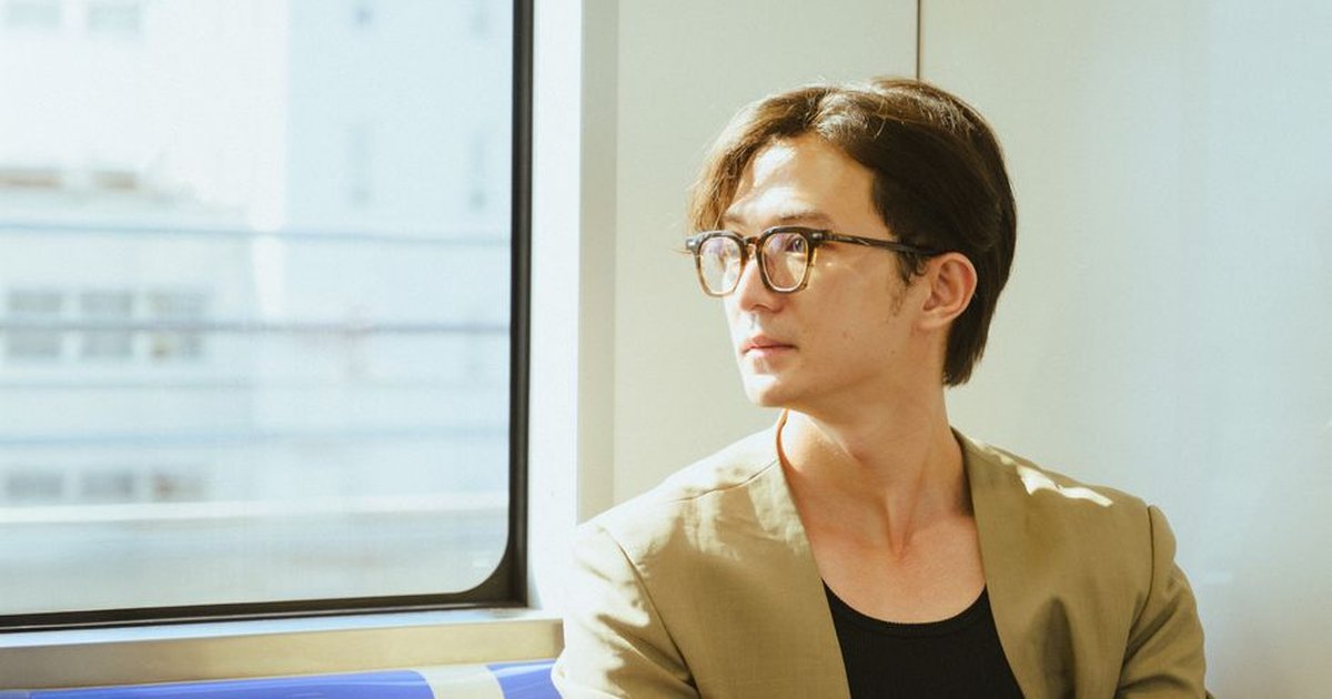 Young man with glasses gazes out a train window on a sunny day.