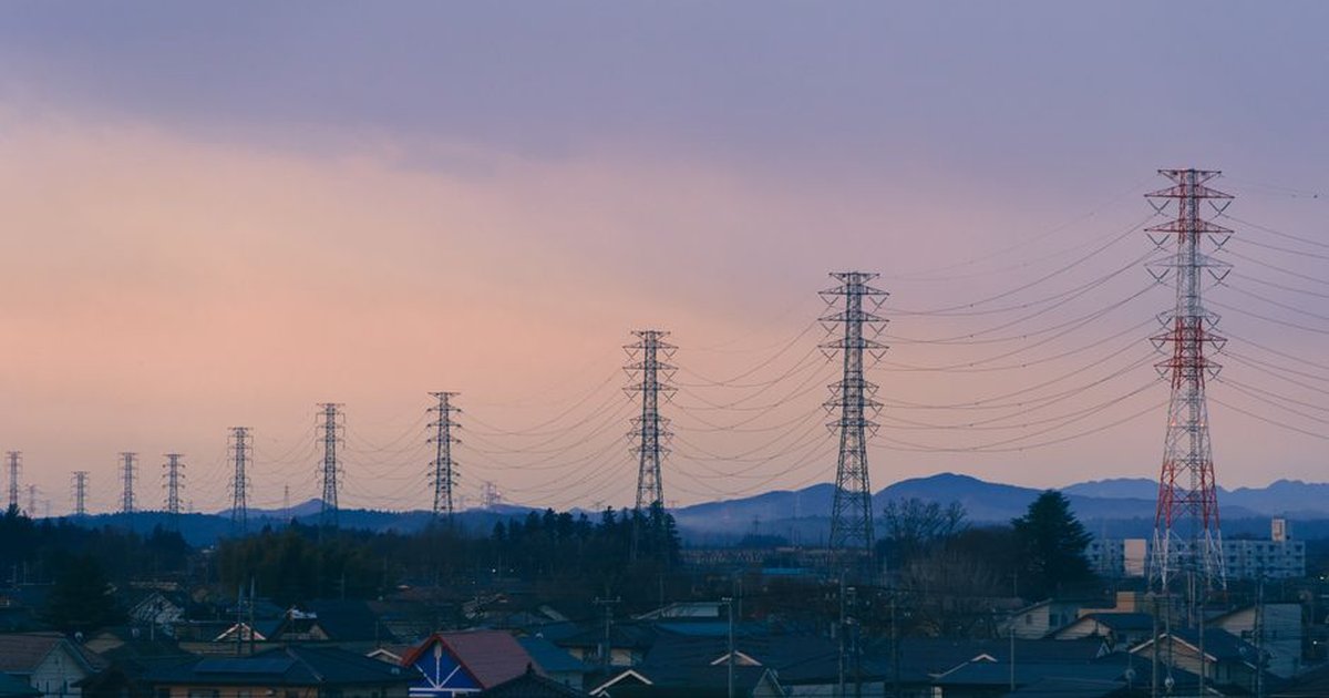 A suburban scene at dusk featuring rows of power lines and distant mountains under a colorful sky.