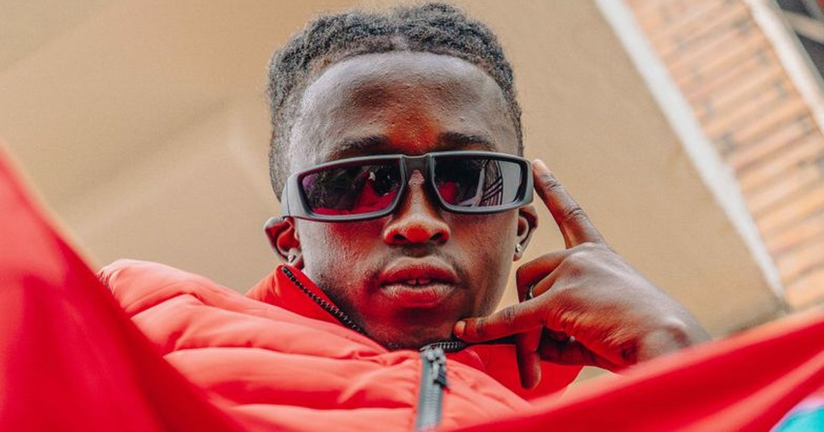 Fashionable young man in a red jacket posing with sunglasses in an urban setting.