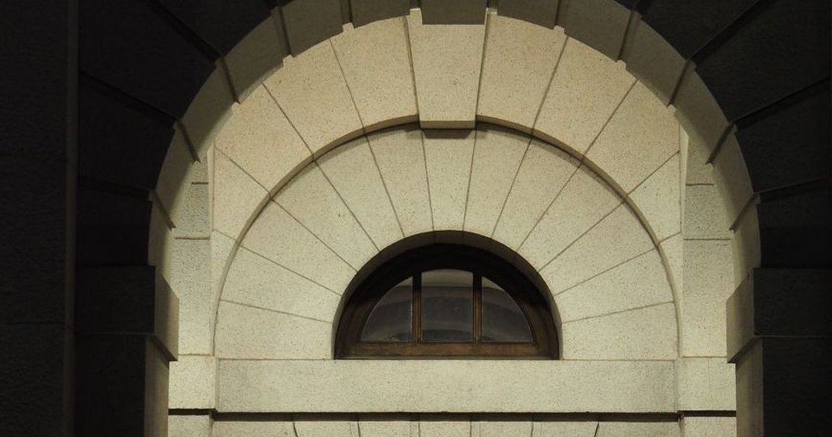 Sunlit stone arch window of a historical building facade in Hong Kong, showcasing classic architecture.