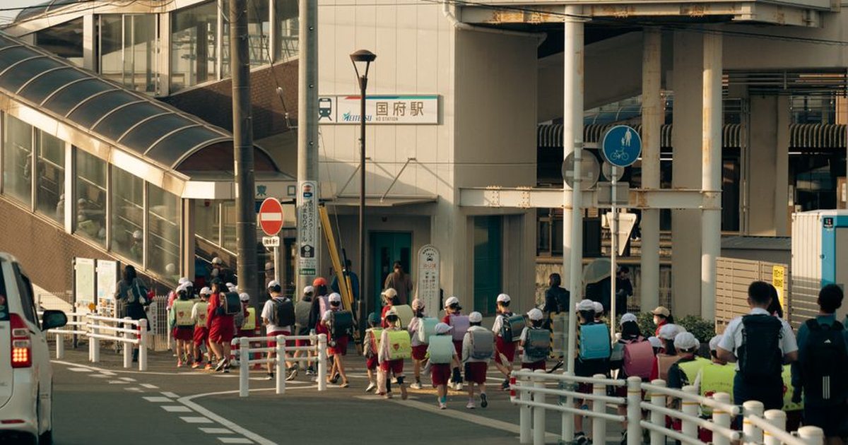 Group of children with backpacks walking towards train station in Toyokawa, Japan, during daytime.