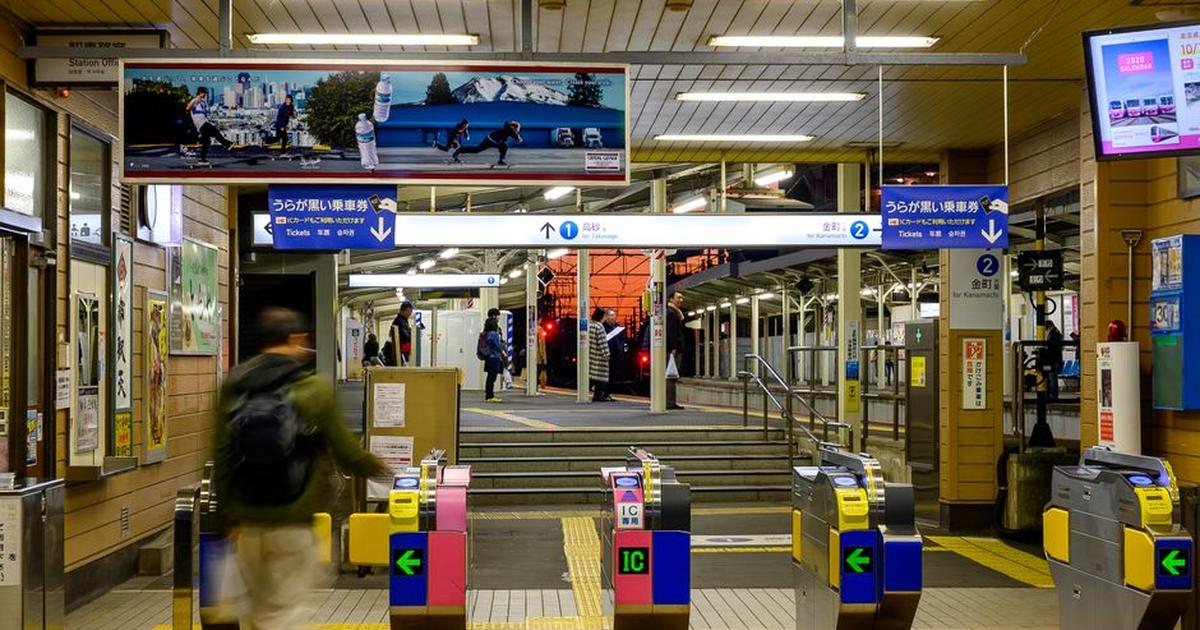 A busy evening scene at a Japanese train station featuring ticket gates and passengers entering the platform area.