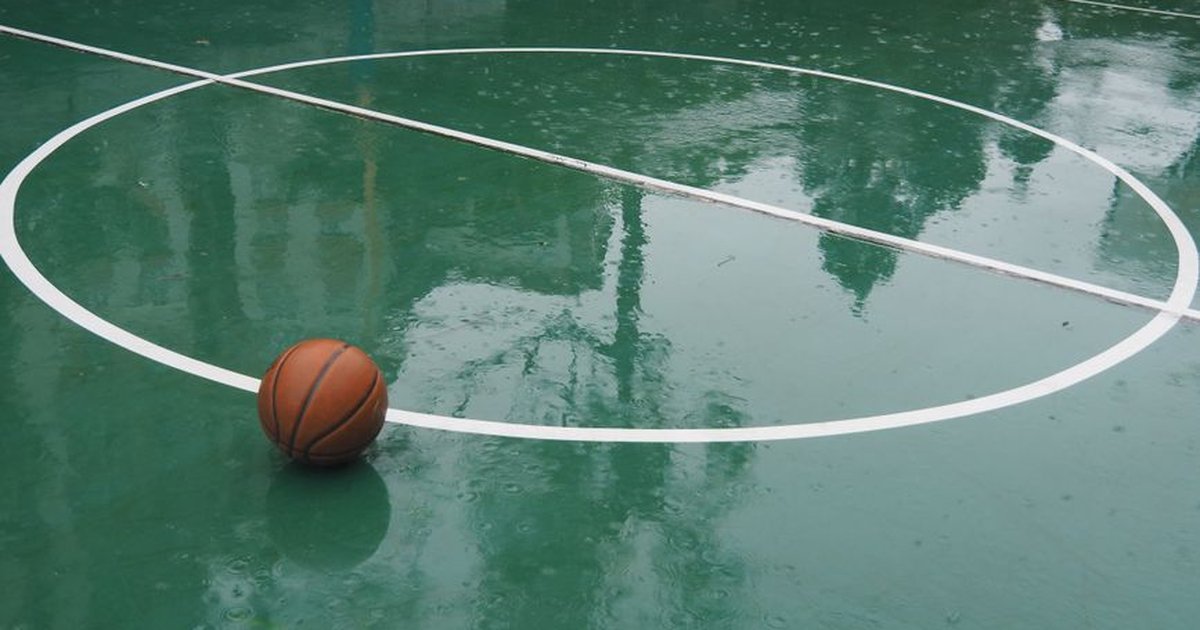 A basketball sits on a rain-soaked court in Hong Kong, reflections visible on the wet surface.