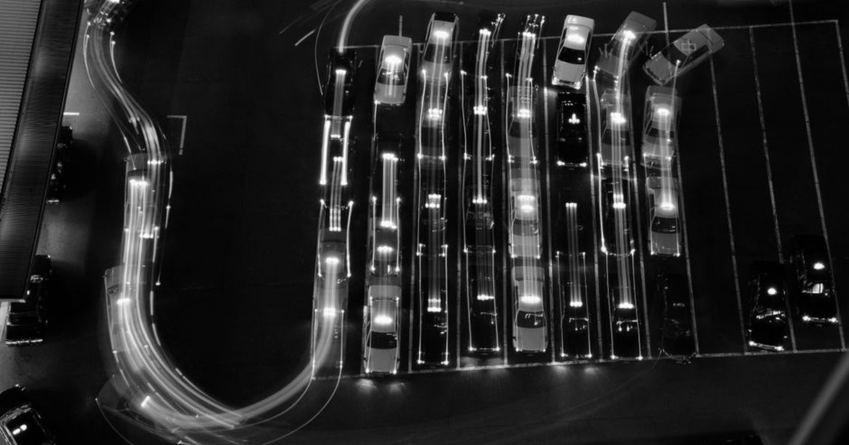 Aerial view of light trails in a parking lot at night, featuring moving vehicles and cars parked in rows.