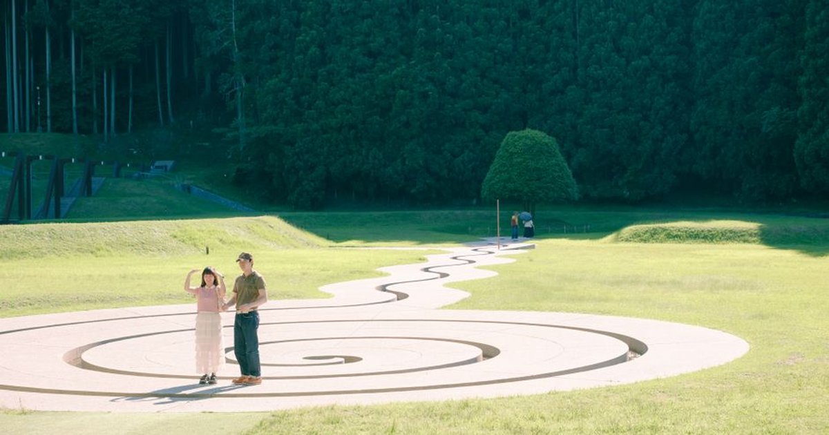 A couple enjoying a sunny day at a spiral walkway in a Japanese park with lush greenery.