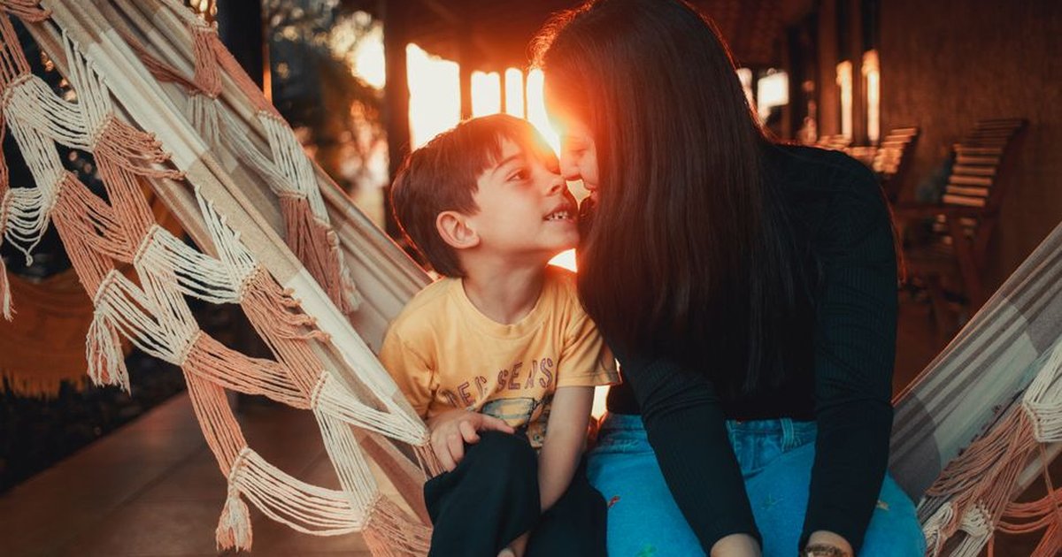 A touching moment between a mother and son sitting on a hammock, smiling at sunset.