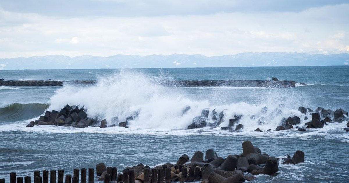 Dramatic ocean waves crashing on tetrapods under a cloudy sky. A coastal scene showcasing sea defense structures.