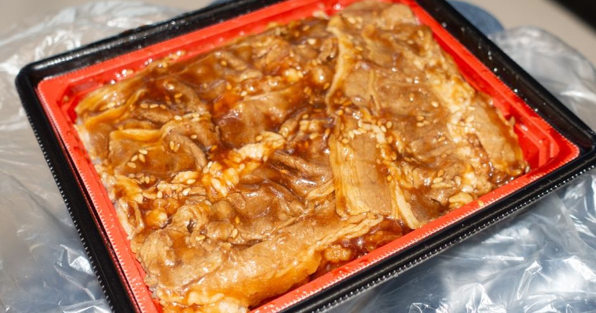 Close-up of pre-marinated meat with sesame seeds in a red tray, ready for cooking.