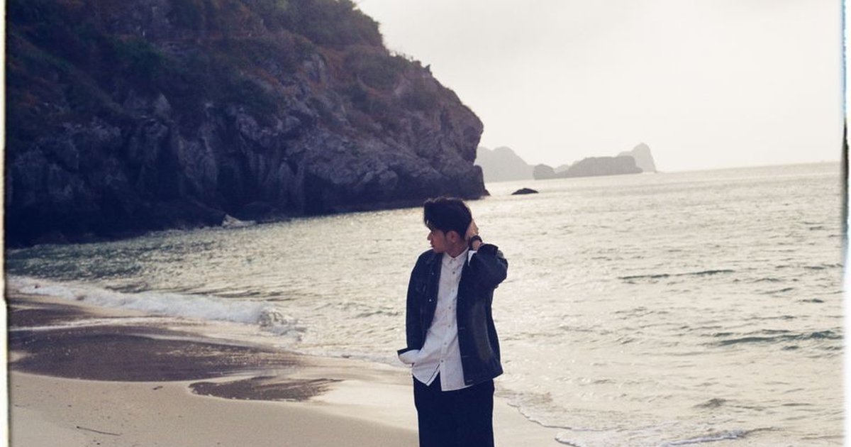 A young adult walking on a quiet beach with rocky cliffs, exuding a peaceful morning vibe.