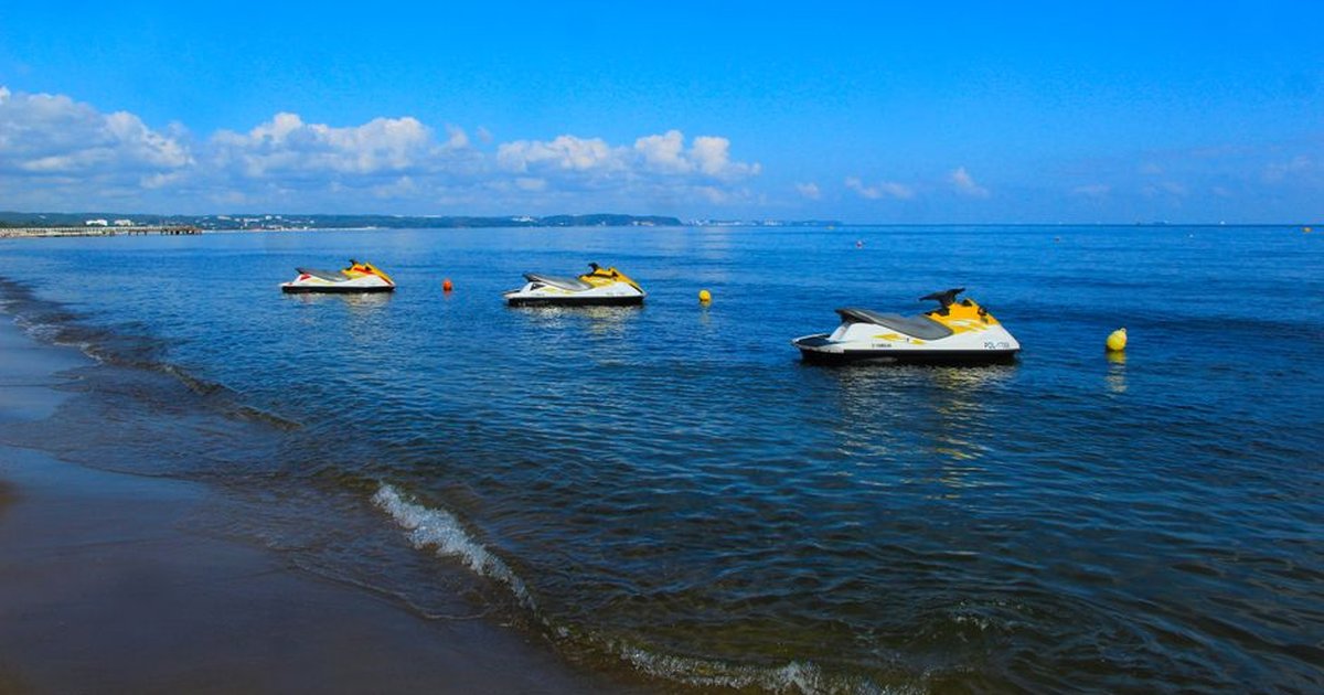 Three jet skis floating on a tranquil beach under a sunny blue sky.