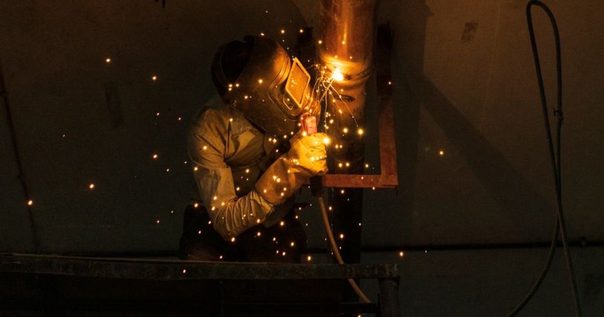 A welder at work indoors, creating bright sparks while welding metal pipes.