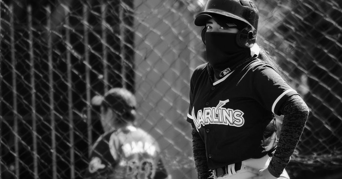 Unrecognizable baseball player in uniform wearing a helmet and facemask, captured in black and white.