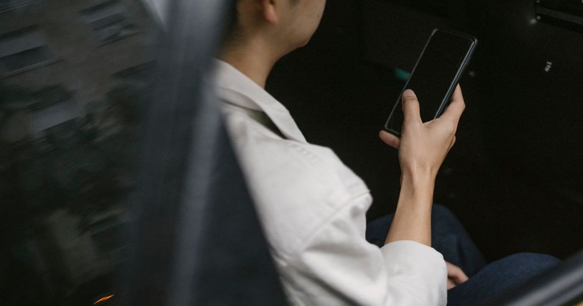 From above of crop unrecognizable male passenger in eyeglasses and casual outfit sitting on backseat and checking information on smartphone