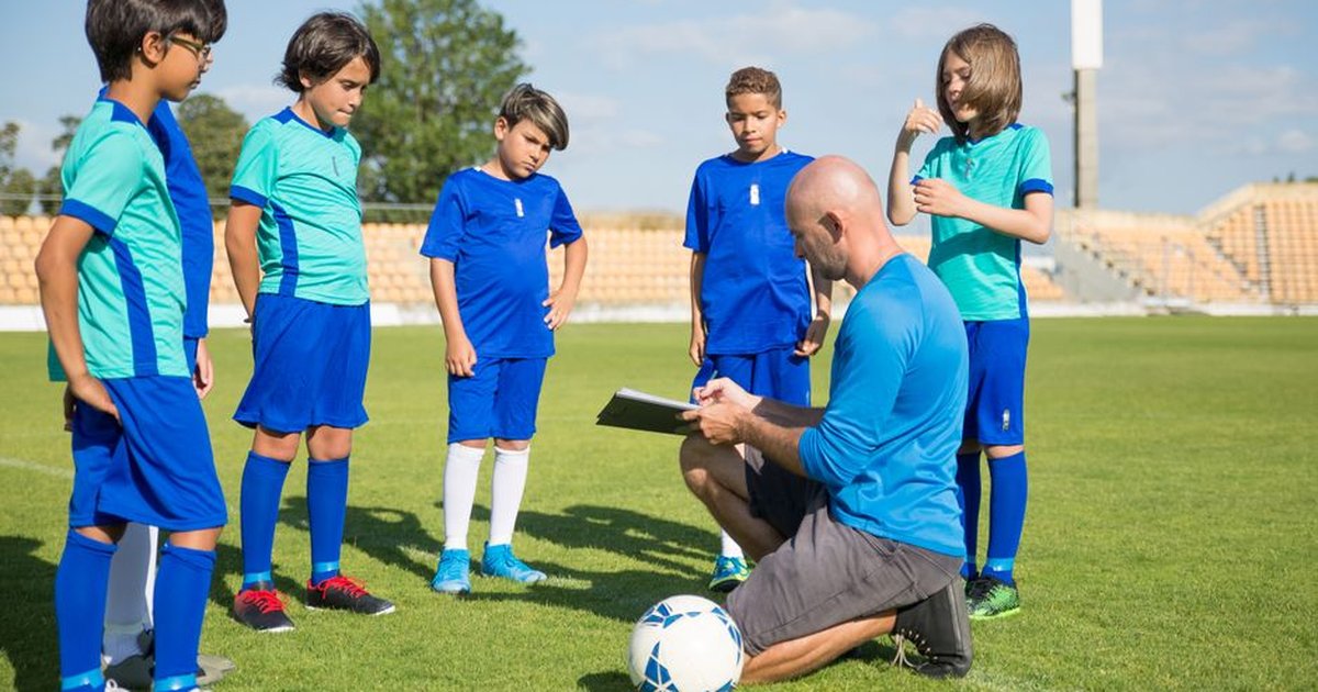 Coach guiding young soccer players on a lush green field under a clear sky.