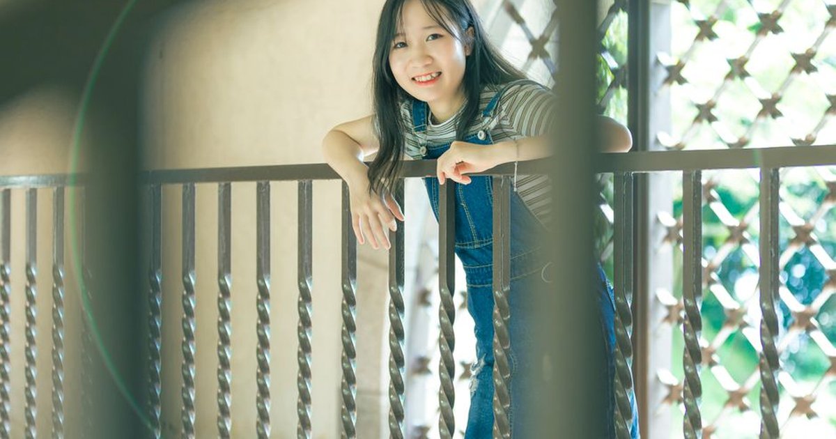 A cheerful young woman leaning on a balcony railing, enjoying the sunny day.