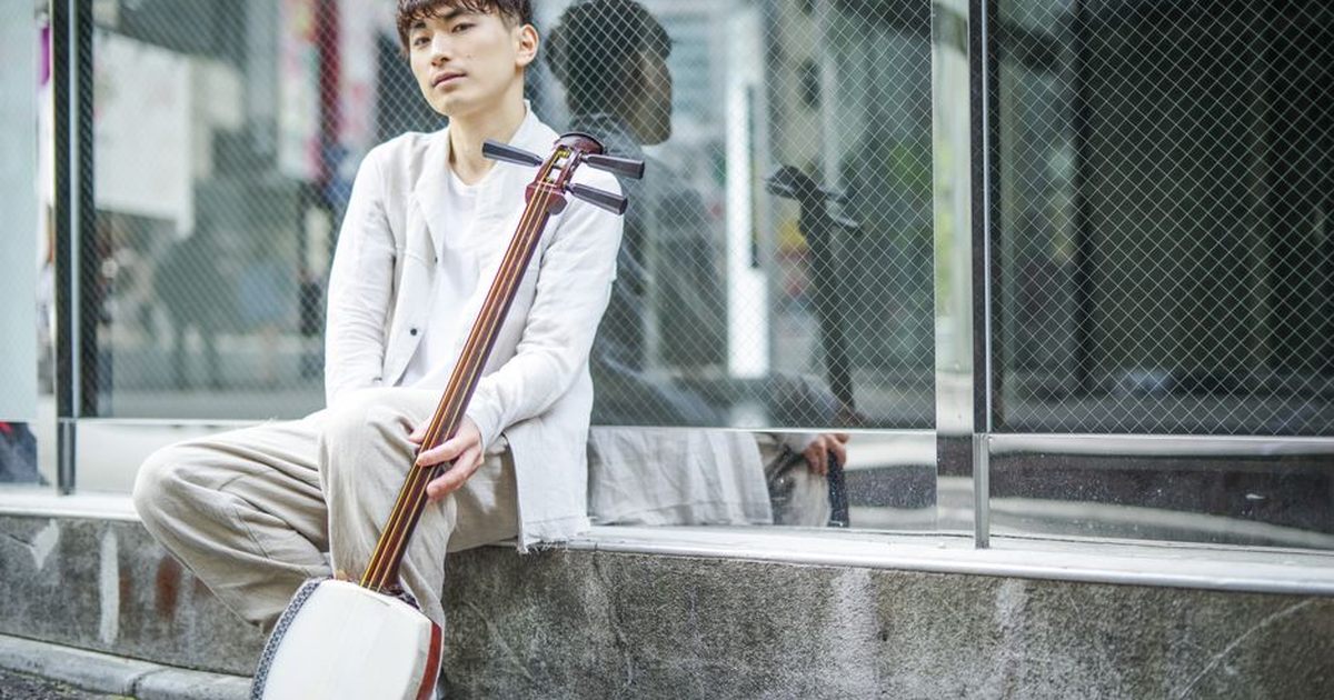 A young man sitting on a street, playing a shamisen, reflecting modern urban culture.
