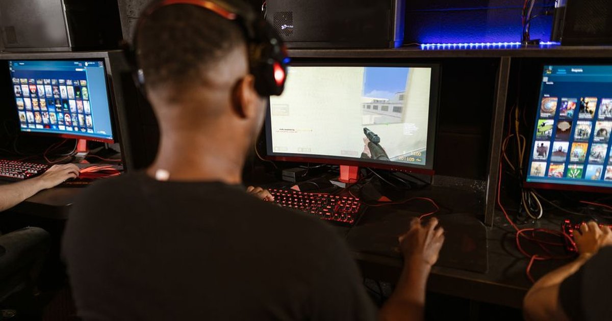 A man deeply engaged in a video game at a modern esports setup with multiple screens.