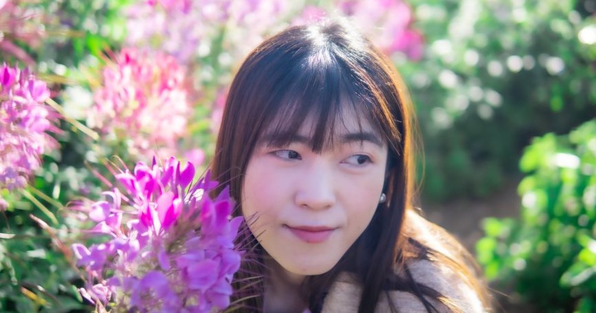 A young woman surrounded by vibrant pink flowers on a sunny day, creating a serene and joyful atmosphere.