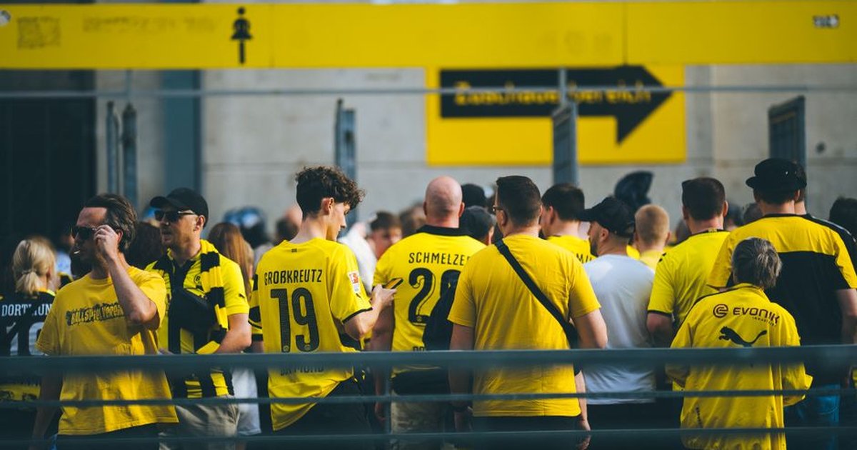 A vibrant crowd of football fans in yellow jerseys gathered at a stadium entrance during the day.