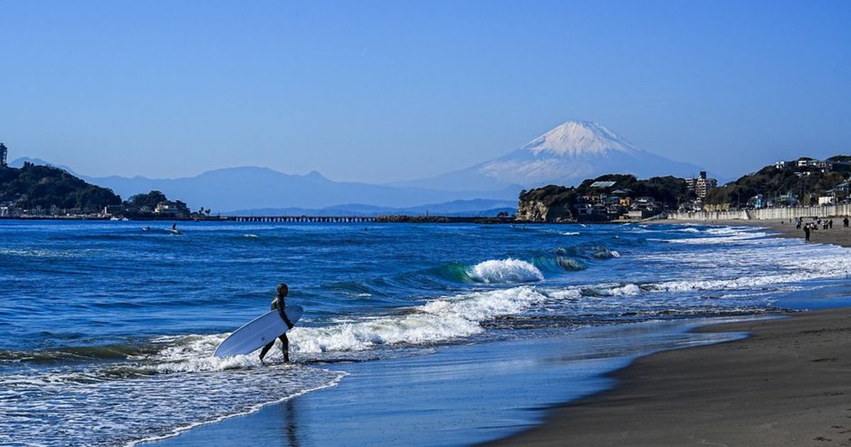 Surfer enters the ocean with Mount Fuji in the background at a beach in Kamakura, Japan.