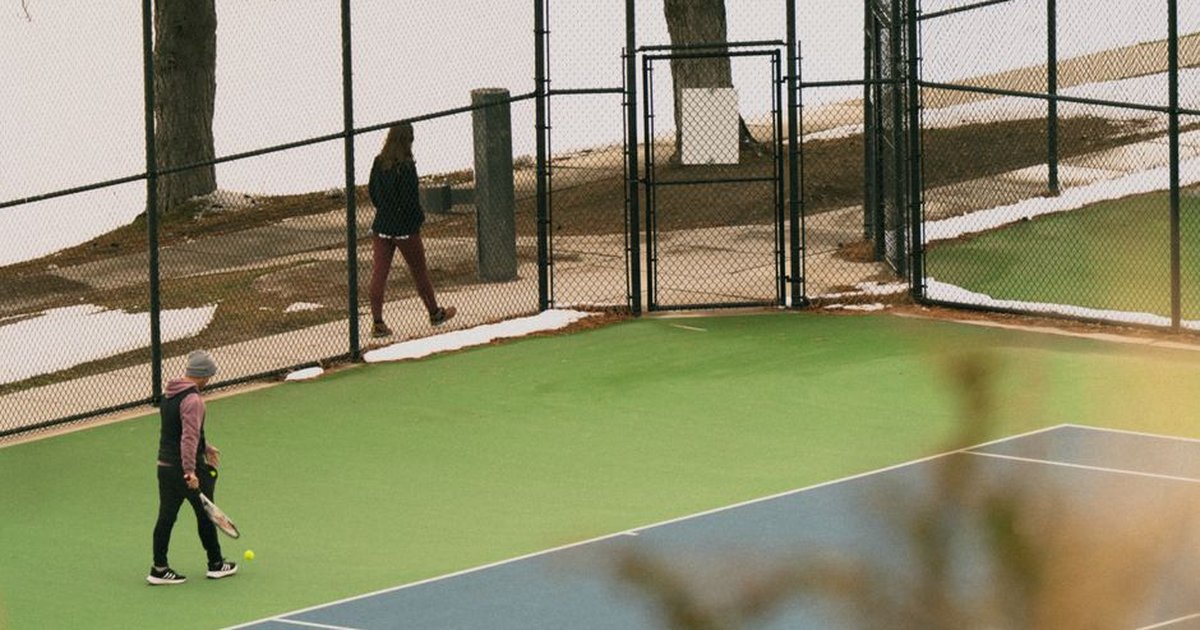 Tennis match in Salt Lake City amidst snow during spring, featuring players on a vibrant court.