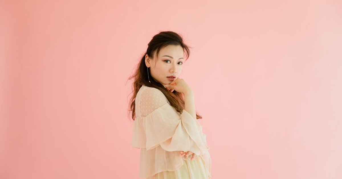 Beautiful woman posing gracefully with a stylish outfit against a pink background.