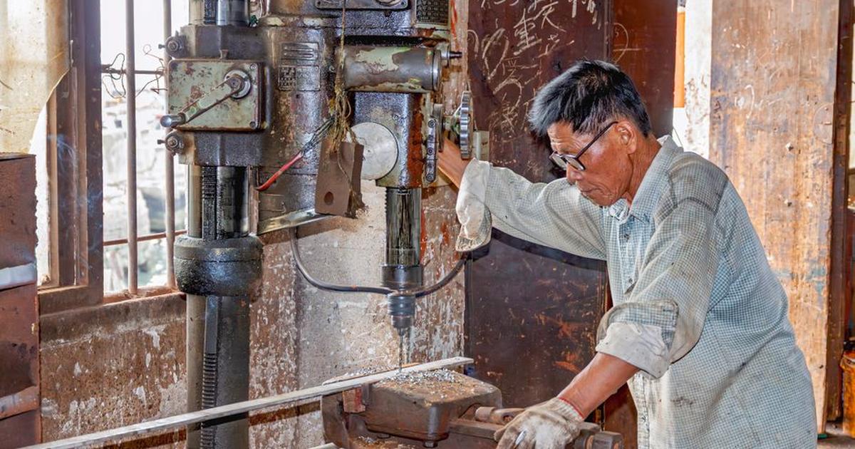 A senior adult man using a drill machine in an industrial workshop setting in Guangdong, China.