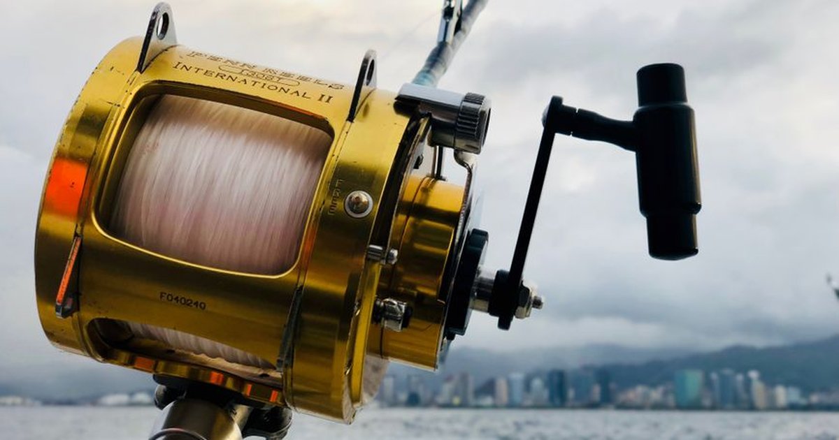 Close-up of a fishing rod and reel over the ocean with the Honolulu skyline in the background.