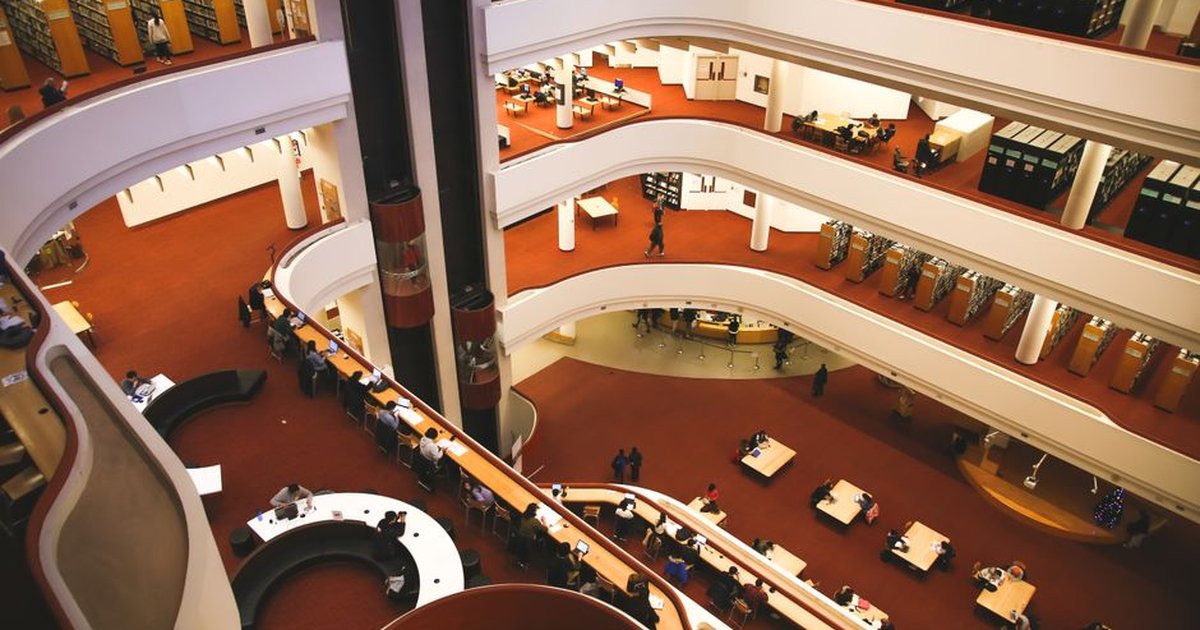 From above of unrecognizable people reading books at tables in spacious halls and atrium of aged Toronto Reference Library