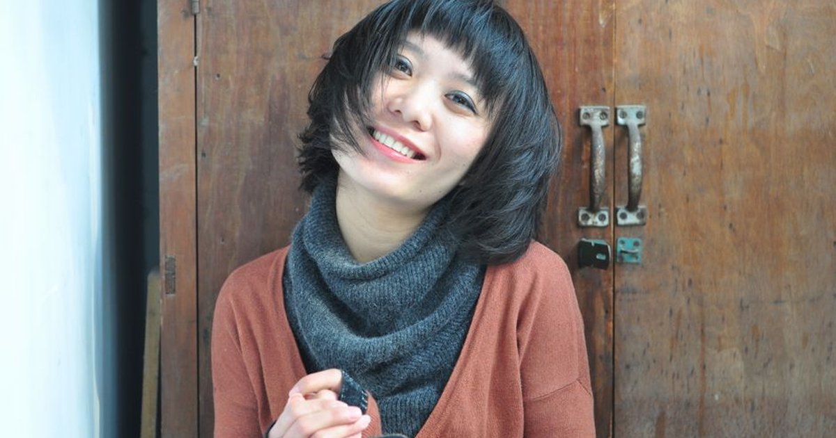 A cheerful woman in casual knitwear sits joyfully indoors.