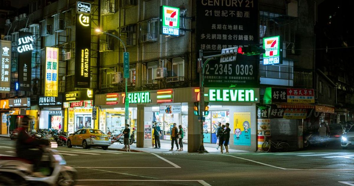 Night view of a bustling 7-Eleven store with vibrant city lights and street activity.
