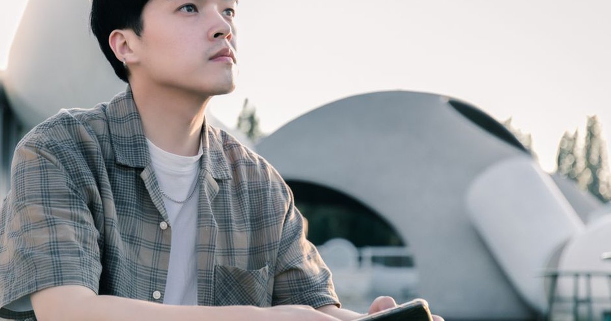 A young man gazes thoughtfully at modern architectural structures in an outdoor setting.