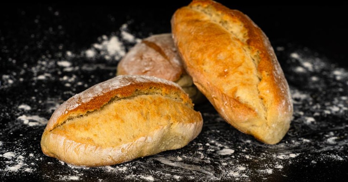 Close-up of artisan bread loaves with flour on a dark surface, highlighting texture and freshness.