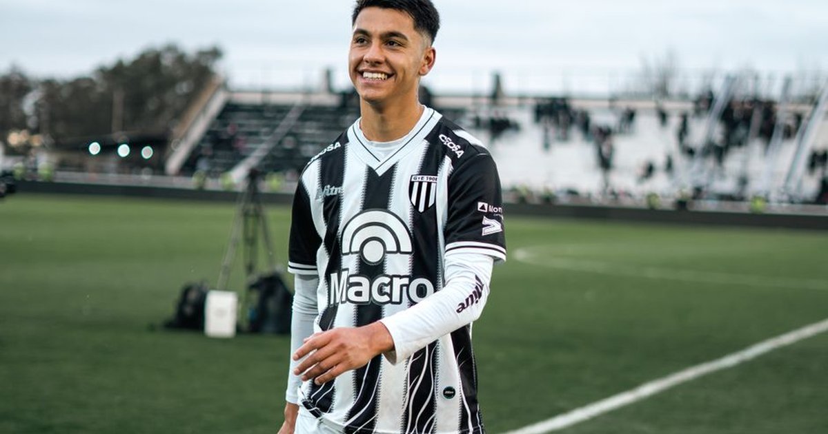 Young soccer player in team uniform smiling during a match on a field.