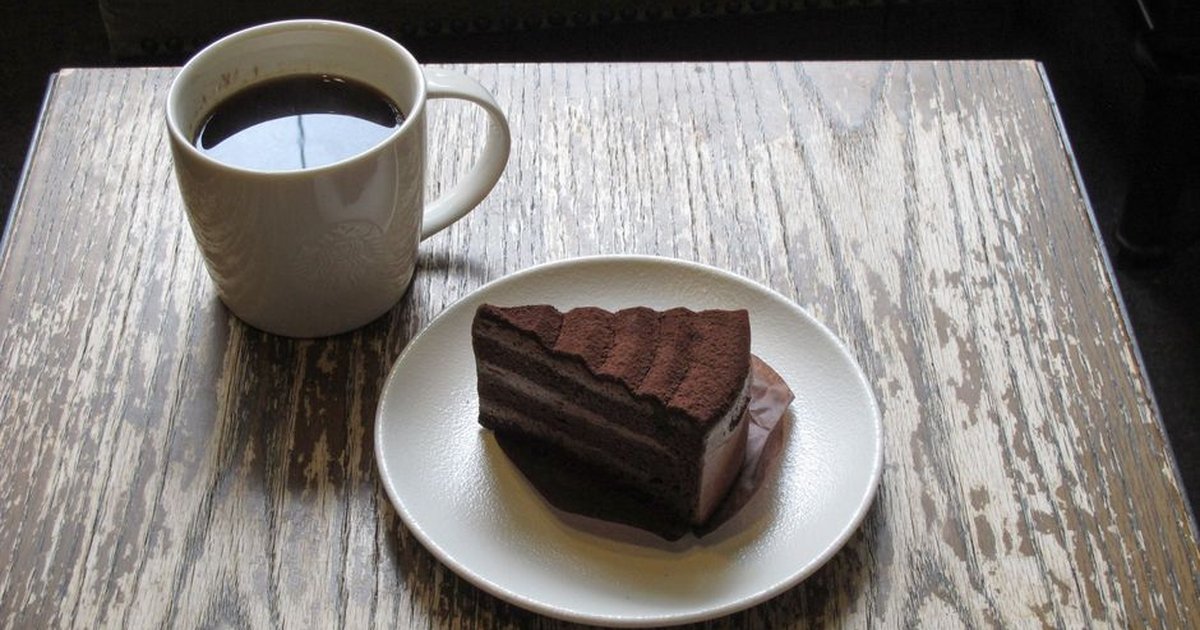 Delicious chocolate cake slice with black coffee on a rustic wooden table, ideal for cozy moments.